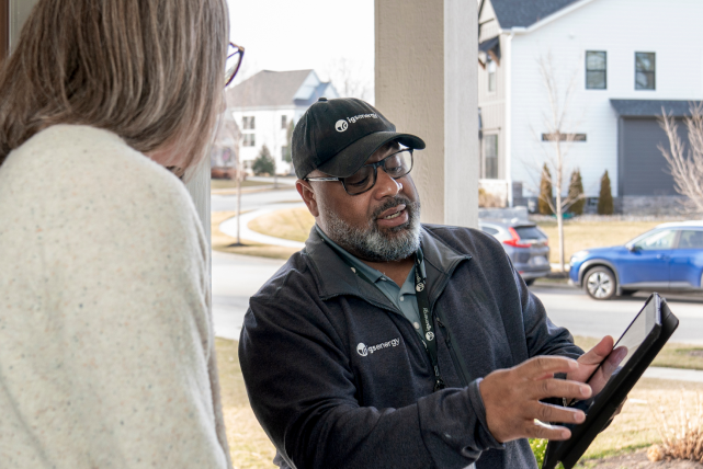 An IGS Energy employee using a digital tablet to review information at a homeowner's front door